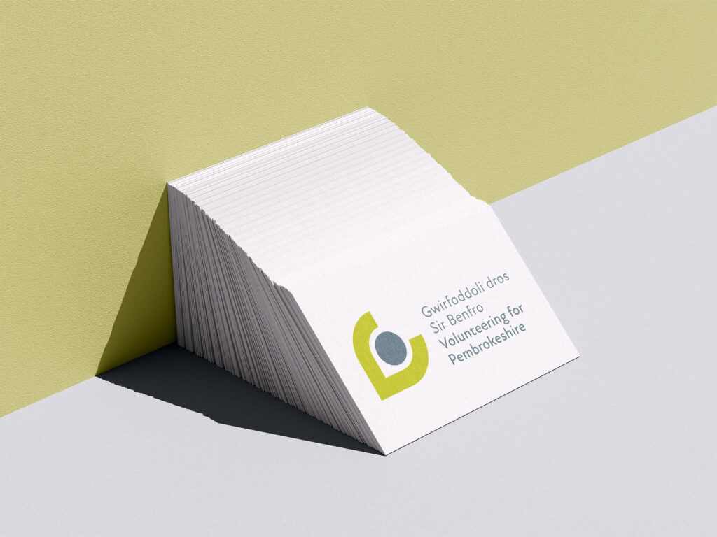A white and green diagonally split background with a stack of white business cards with the Volunteering for Pembrokeshire logo