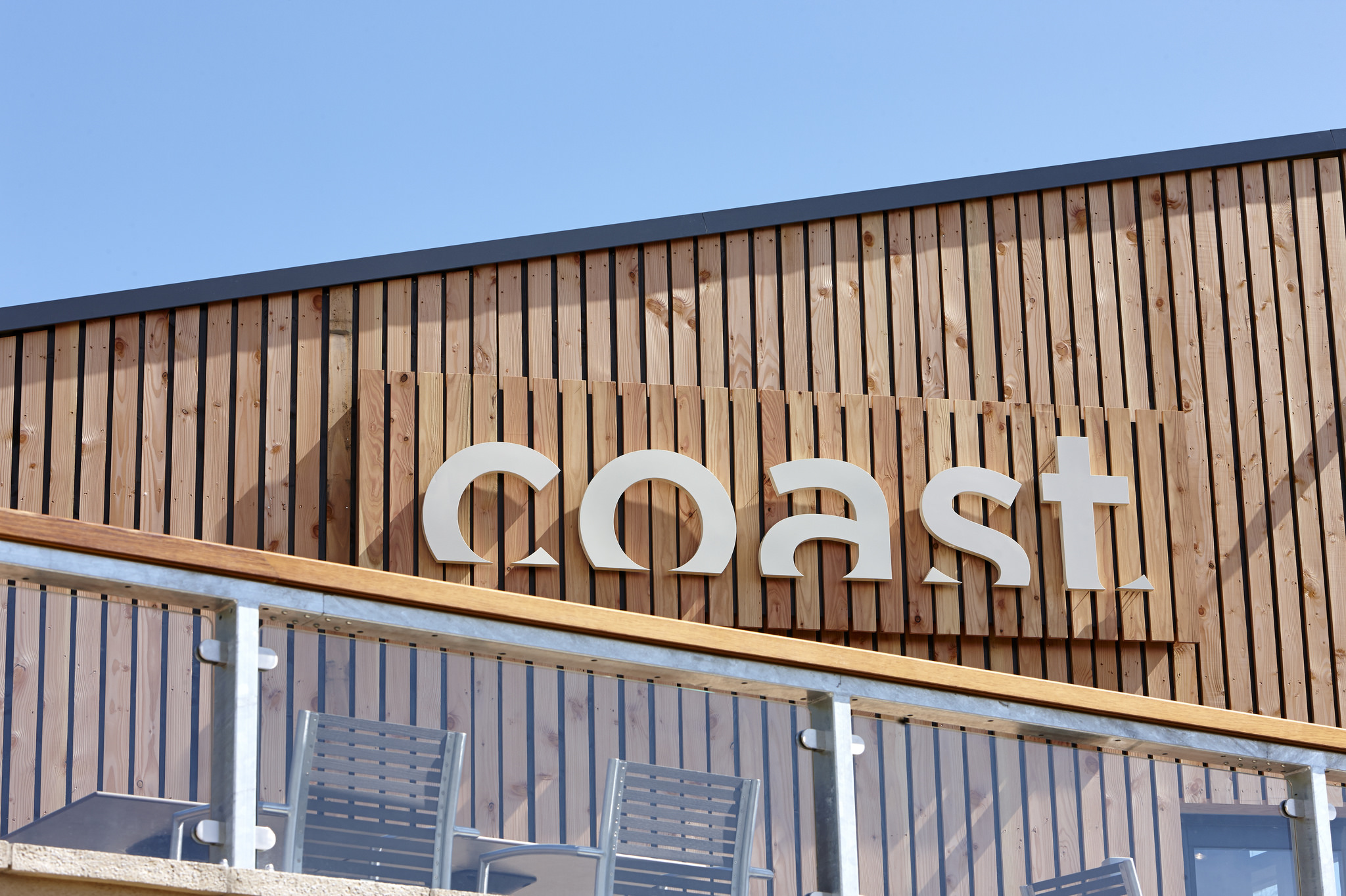 An exterior shot of Coat Restaurant with vertical wooden slats and the Coast logo on a sign