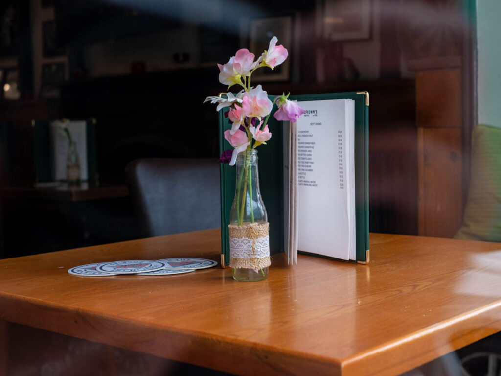 A table at a hotel restaurant with flowers in a glass bottle, and a dark green menu