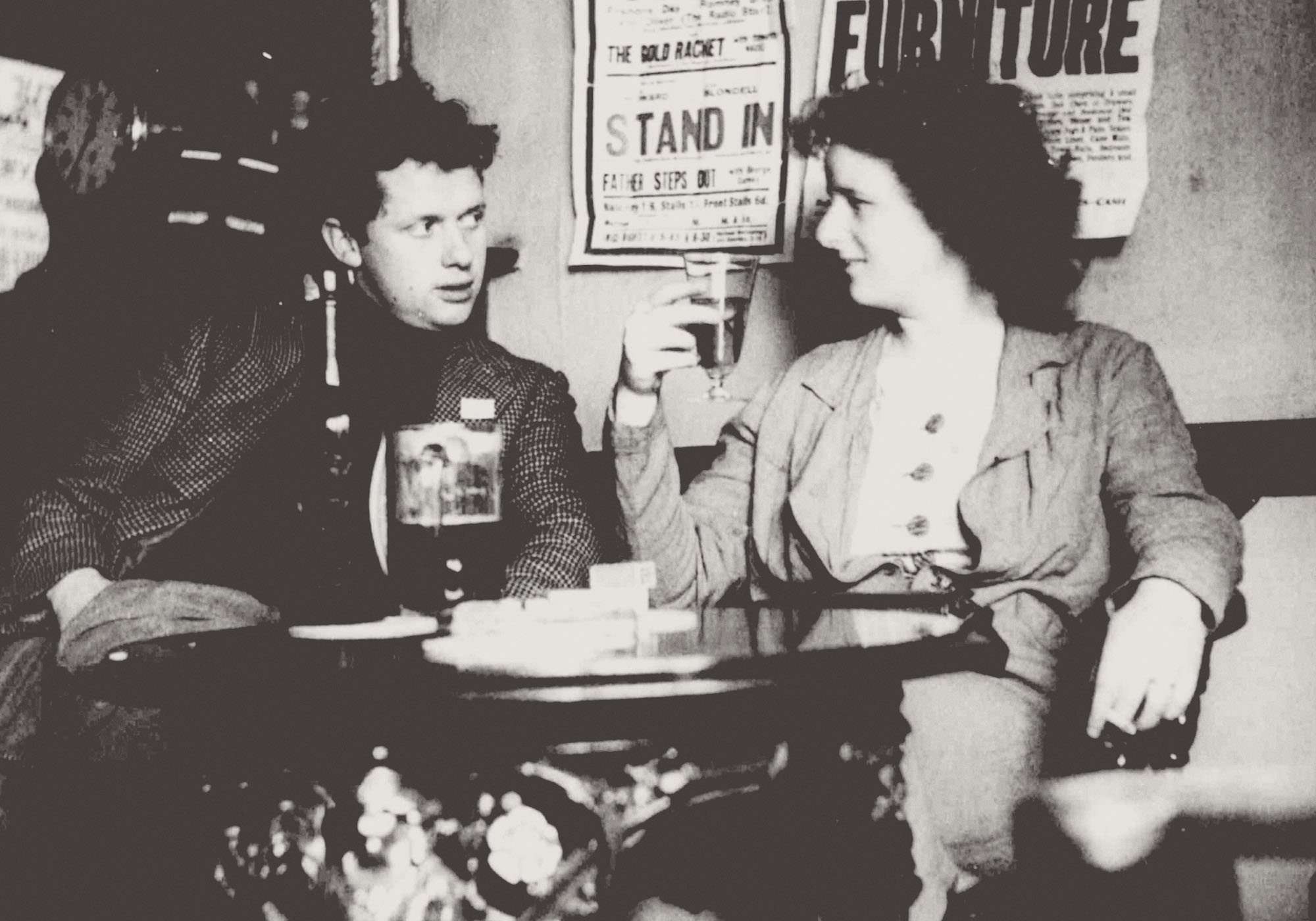 A black and white image of two people sat in a bar looking at each other