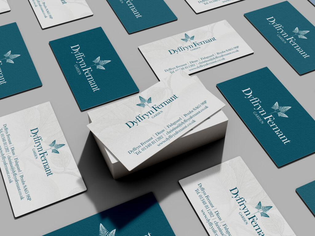 A stack of business cards surrounded by more businesses cards laying flat; the business cards are either white with a teal version of the logo, or teal with a white version of the logo