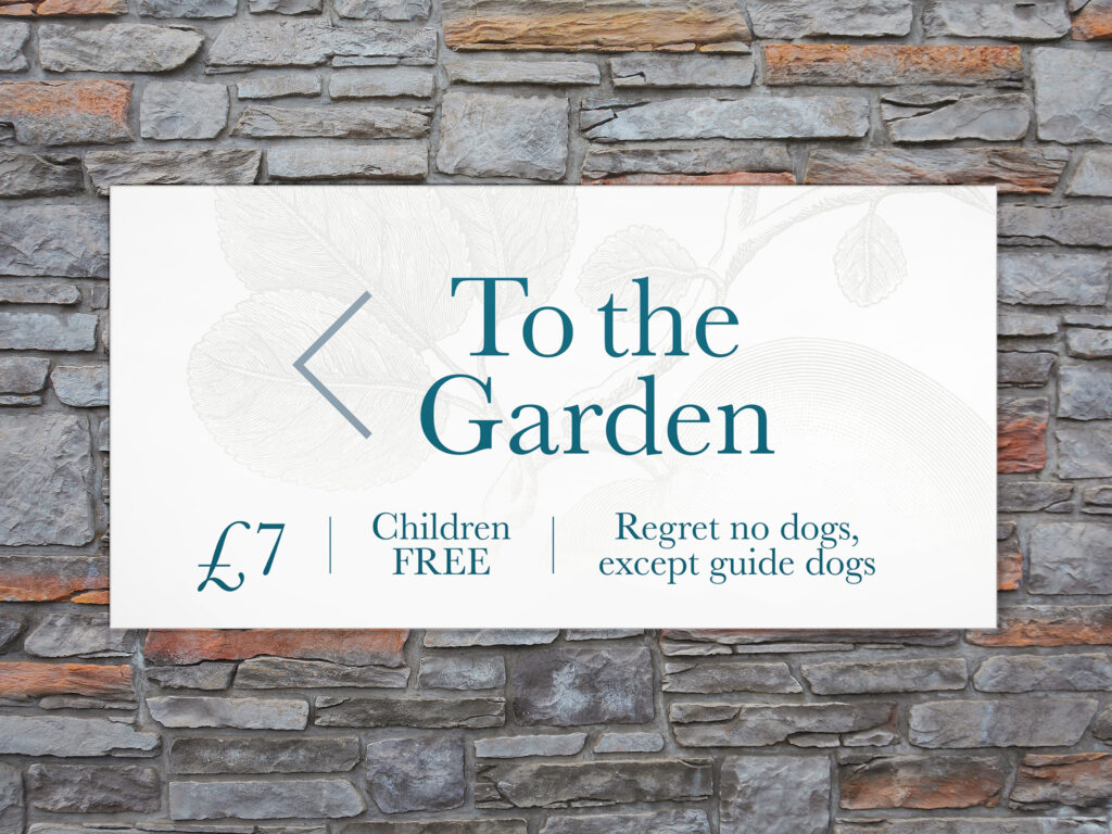 A stone wall with a white sign saying 'To the Garden' written in teal