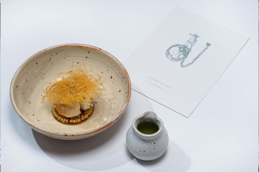 A table set with a white cloth with a bowl and jug, and a card with illustration on it