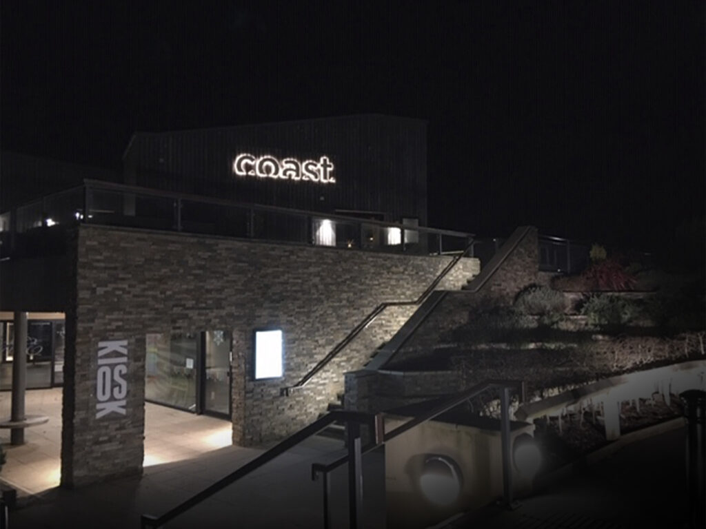 A night time shot of the exterior of the building showing the Coast sign lit up