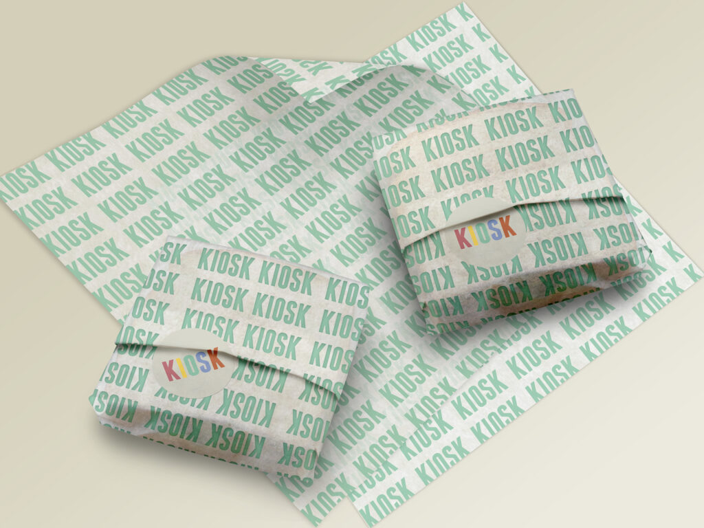 Two sandwiches wrapped in paper with KIOSK written across in mint green laying on more sheets of wrapping paper on an off-white background