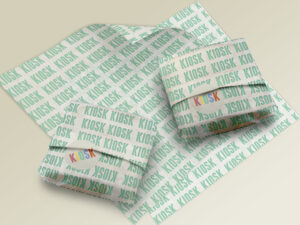 Two sandwiches wrapped in paper with KIOSK written across in mint green laying on more sheets of wrapping paper on an off-white background