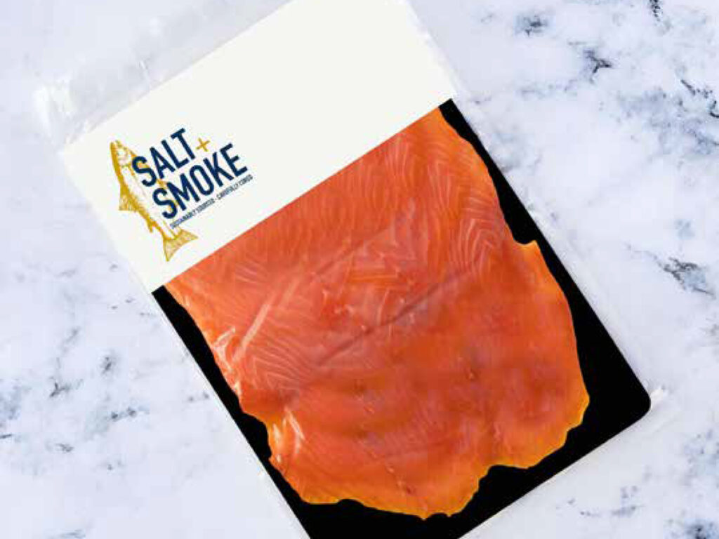 Smoked salmon packaging design on a marble background with a white label and blue logo with gold salmon illustration