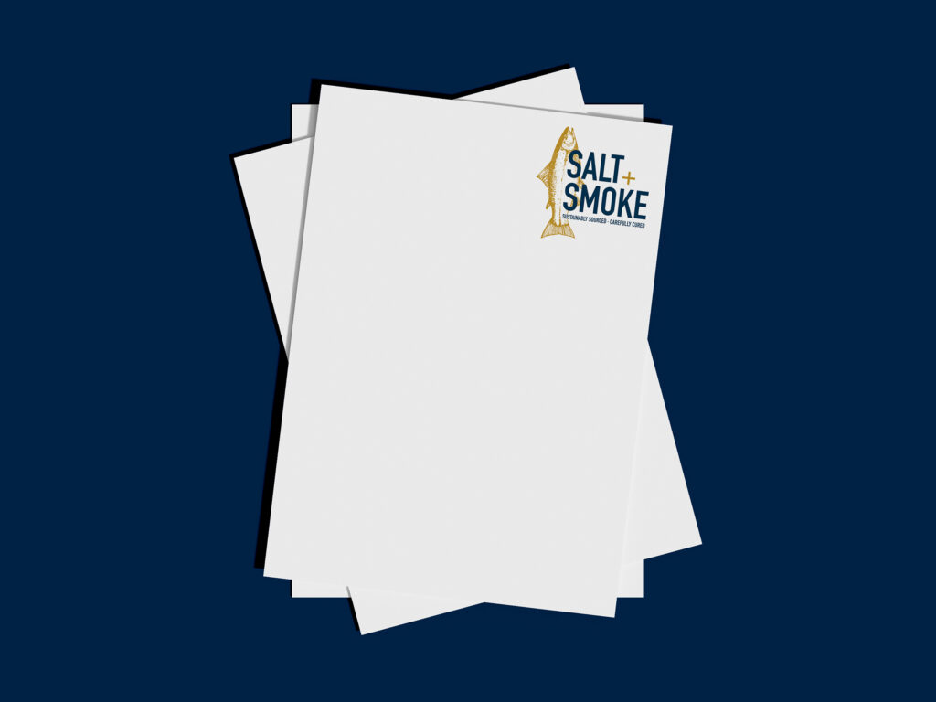 A navy background with a stack of white letterheads with the blue and gold Salt + Smoke logo