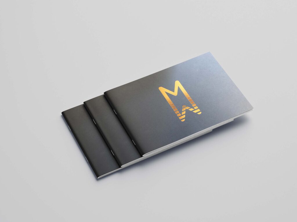 A light grey background with three brochures stacked, with a bronze logo of Milford Waterfront and a dark grey background