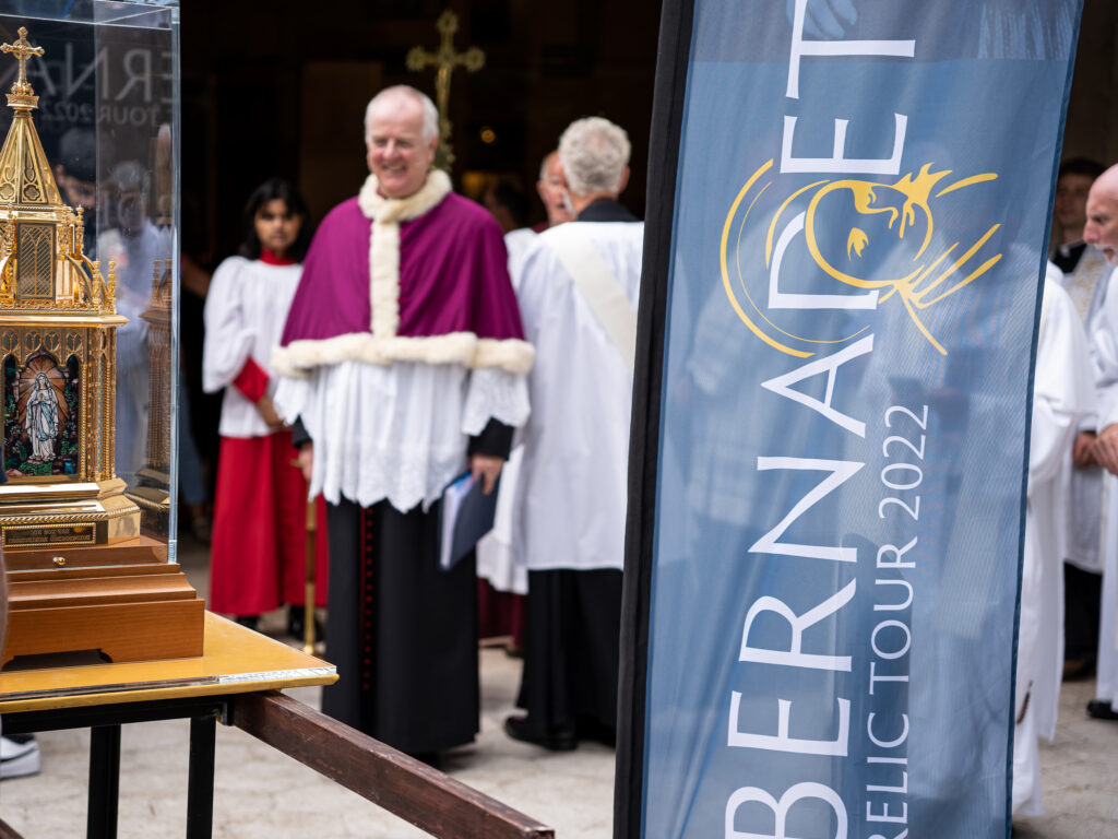 An image showing a blue feather flag with the Saint Bernadette Relic Tour 2022 logo in yellow and white