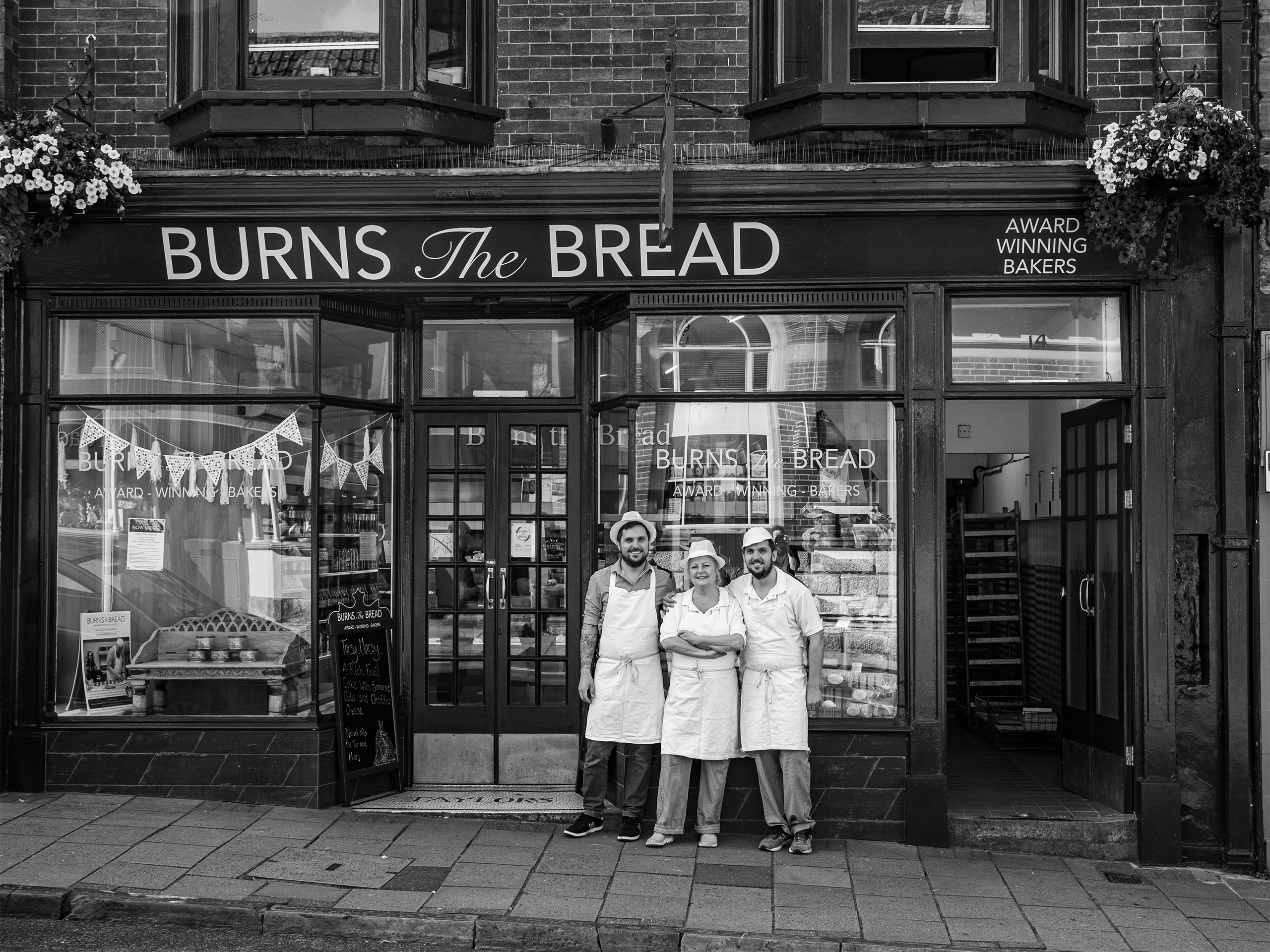 A black and white image featuring a family stood in front of a bakery