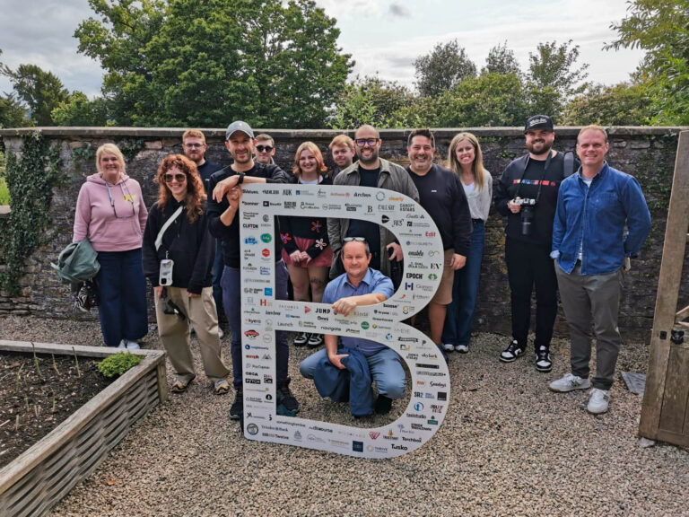 A group of people stood in front of a stone wall with a giant 'B' cut out in front of them