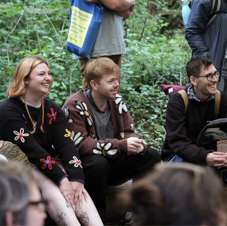 Three people in a group of more people attending a talk, the people are all smiling and laughing