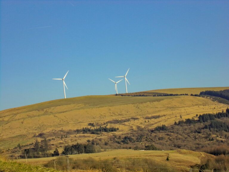 A hill with three wind turbines on top against a bright blue cloudless sky
