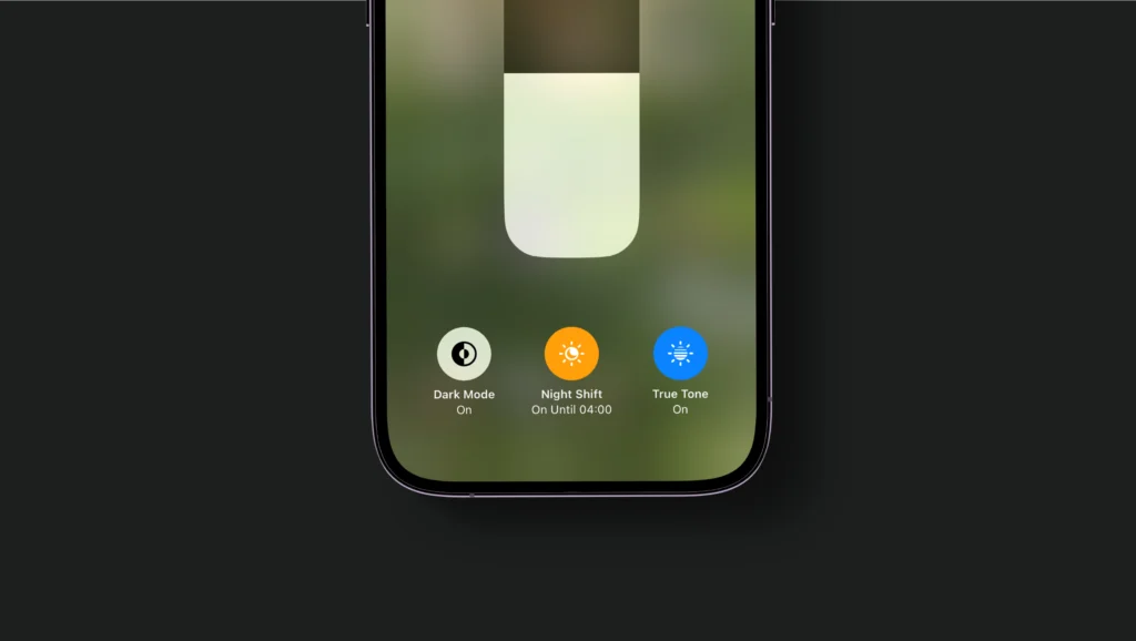 A dark grey background showing the bottom half of an iphone on the brightness setting showing that night mode is switched on